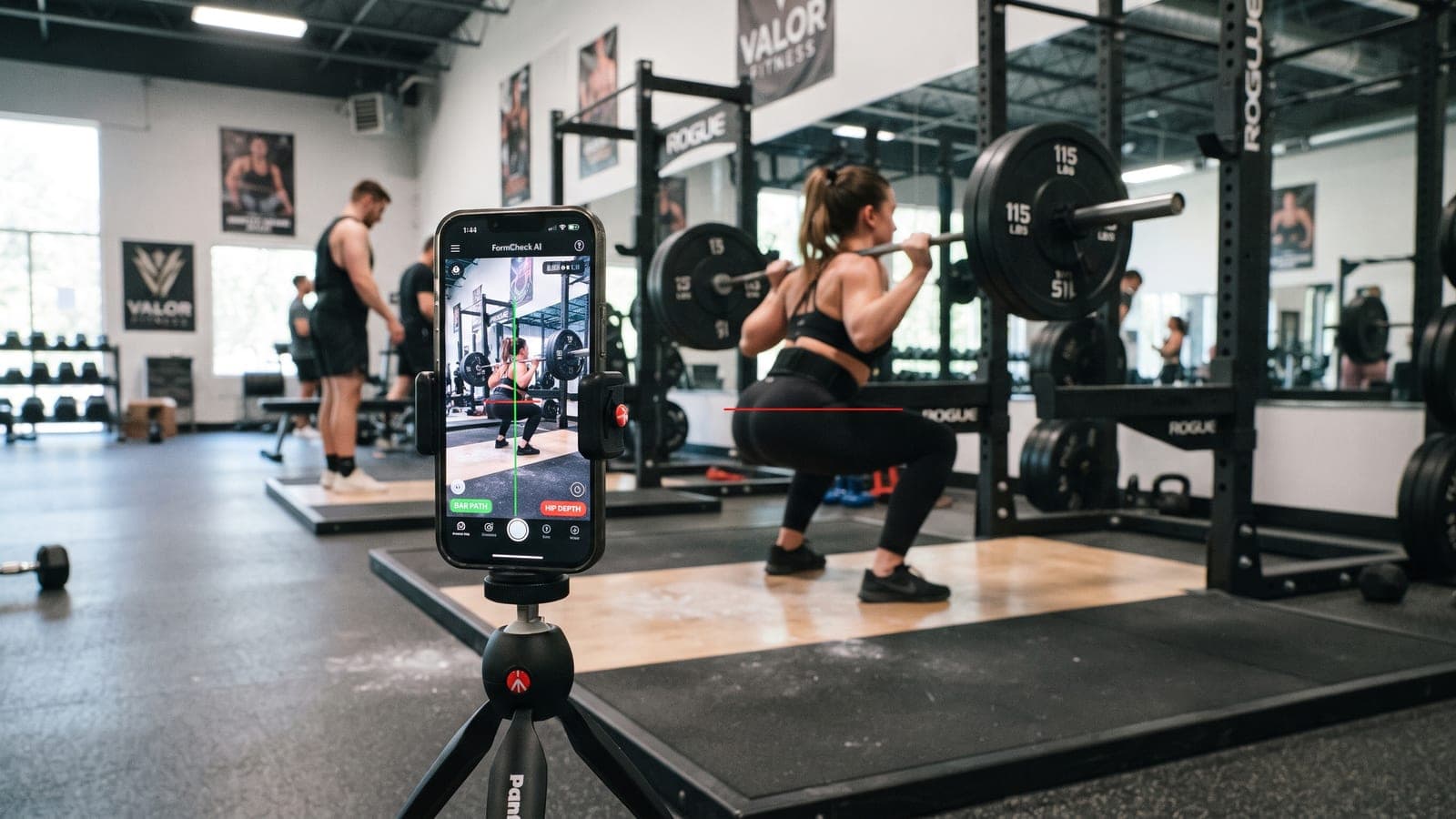 A phone on a tripod filming a lifter performing a barbell squat for form review
